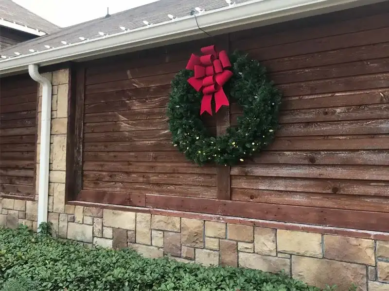 Outdoor Christmas wreath with a large red bow on a wood-sided wall